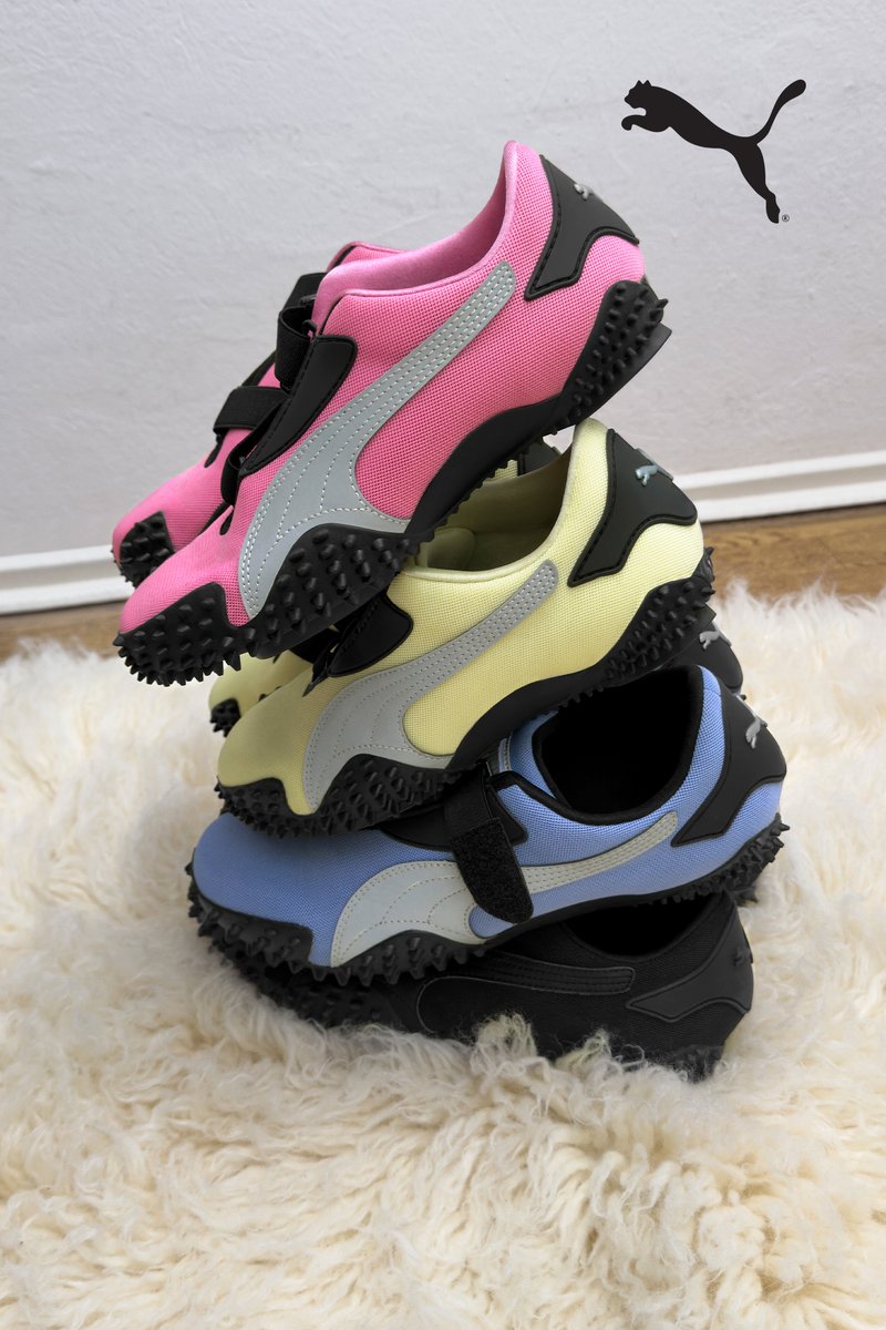 Cuatro zapatillas Puma coloridas apiladas: rosa, amarillo, azul y negro. Tela texturizada, suelas de goma negras con un agarre prominente y correas ajustables.