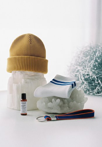 Musztardowy, prążkowany beanie, białe skarpetki w niebieskie paski, mała brązowa butelka z etykietą "Evolve" oraz pasek z niebieskimi i pomarańczowymi akcentami.
