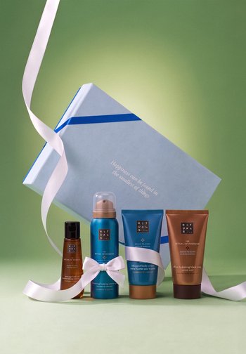 Quatre produits de bain et corps Rituals avec un ruban blanc, à côté d'une boîte cadeau bleue portant l'inscription "Happiness can be found in the smallest of things."