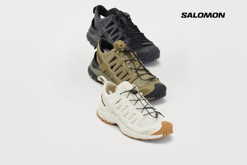 Tre paia di scarpe Salomon sono esposti: nere, verde oliva e bianche con accenti marroni, disposte su uno sfondo chiaro.