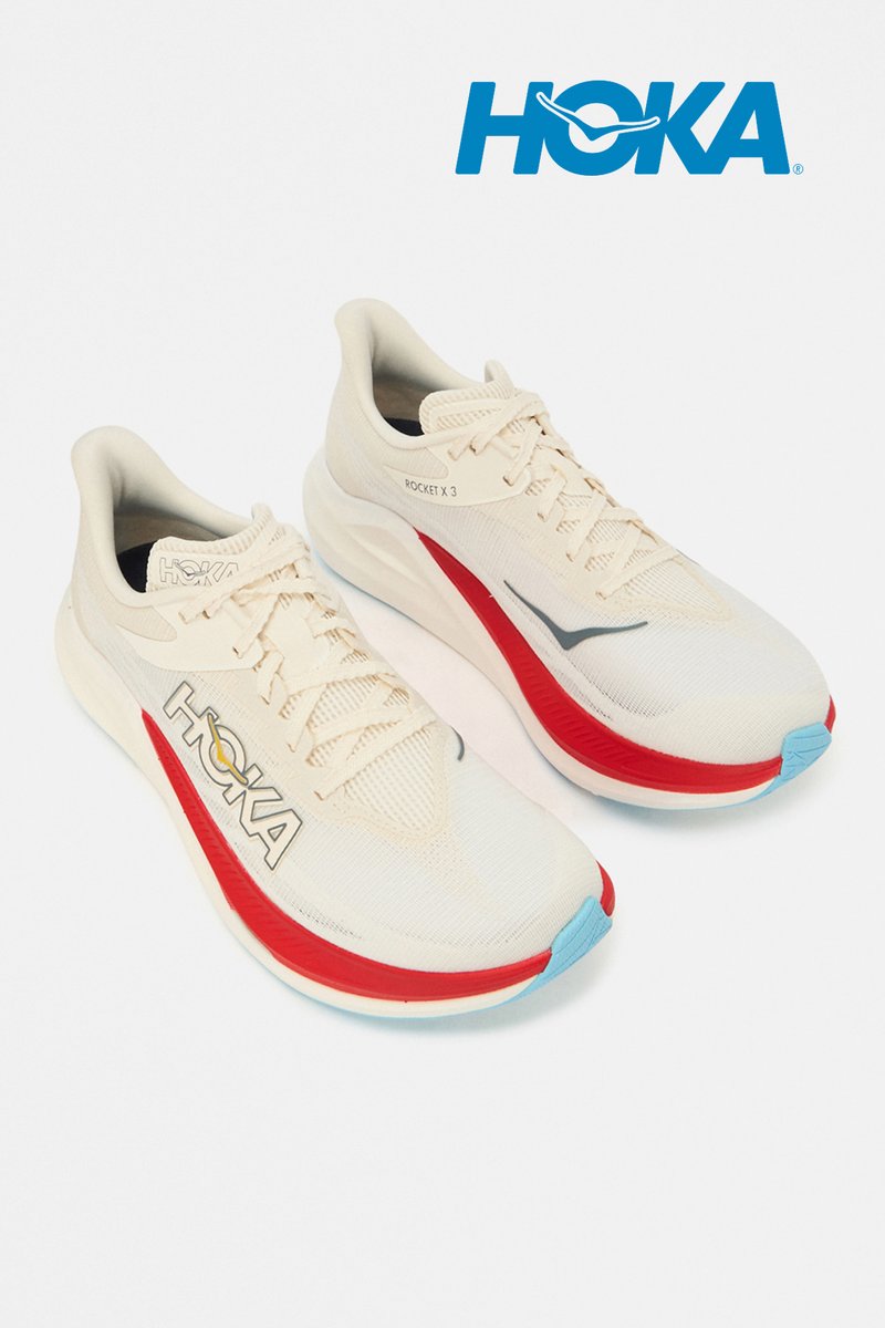 Paar cremefarbener Hoka Rocket X 3 Laufschuhe mit roten und hellblauen Akzenten, nebeneinander gegen einen weißen Hintergrund platziert.