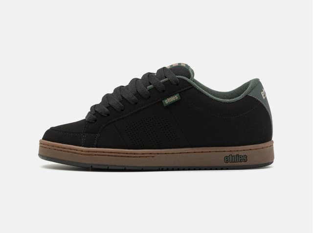 Svart sneaker med grønne detaljer, med perforerte detaljer og brun såle. Merket "etnies" er synlig på siden og hælen.