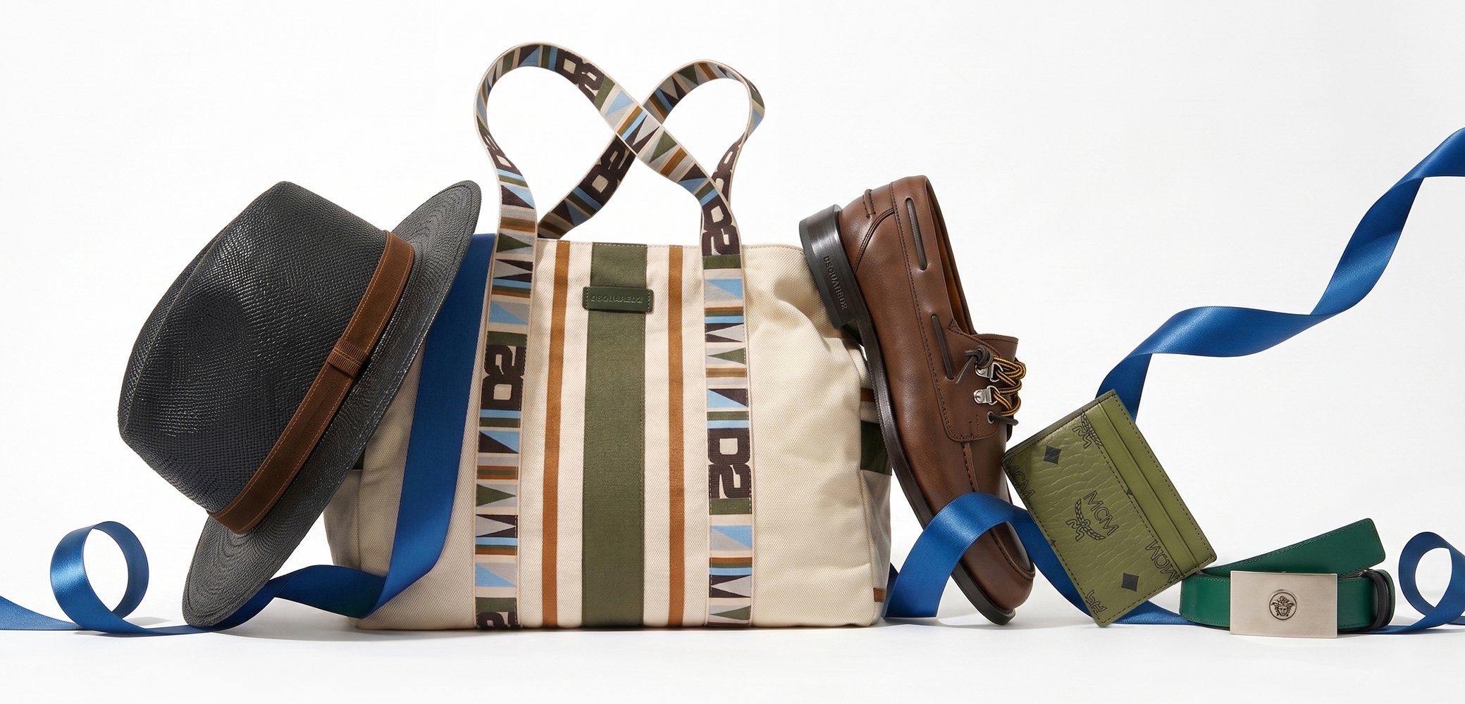Chapeau fedora en paille, sac fourre-tout en toile rayée, chaussure en cuir marron, montre verte dans une boîte et ceinture verte avec un ruban bleu sur fond blanc.