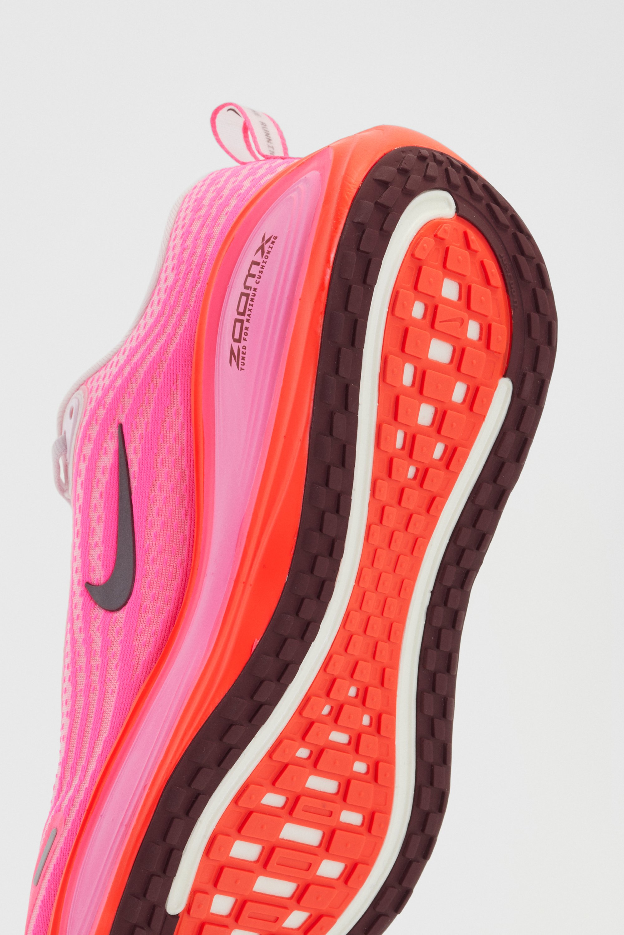 Nike hardloopschoen met een roze mesh bovenwerk, zwart logo en een gestructureerde zool in oranje en bruin met witte accenten.