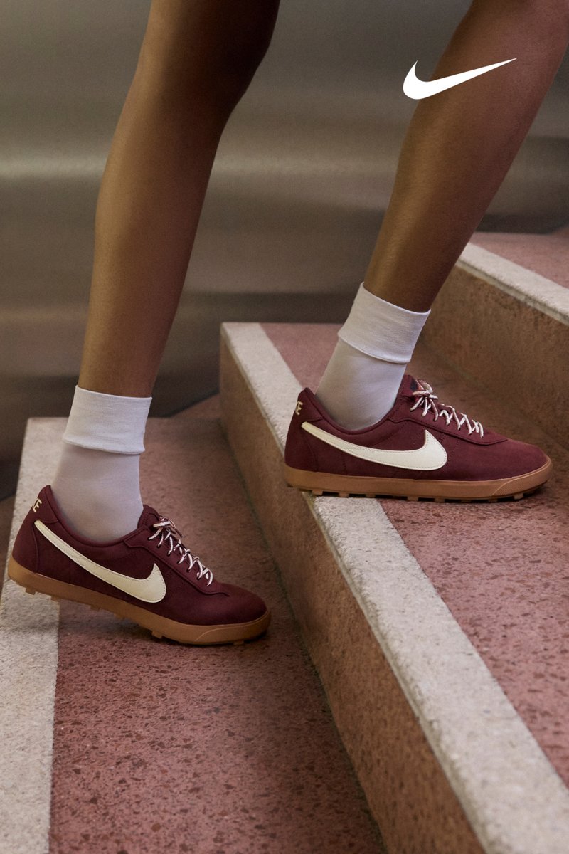 Vinrøde Nike-sneakers i ruskind med hvid swoosh, snørelukning og gummisål, placeret på betontrapper, kombineret med hvide sokker.