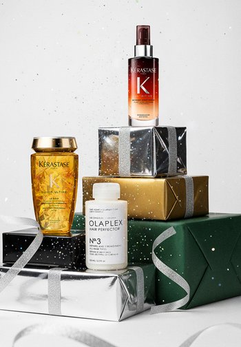 Produkty do pielęgnacji włosów Kérastase i Olaplex na stosie kolorowych pudełek prezentowych. Cechy charakterystyczne: złote, srebrne i zielone opakowania, błyszczące tekstury oraz etykiety.