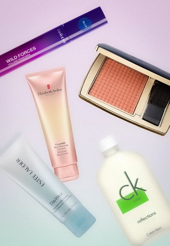 Tube de mascara, poudre blush compacte avec pinceau, tubes de soins pour la peau d'Elizabeth Arden et Estée Lauder, et flacon de lotion Calvin Klein sur fond blanc.