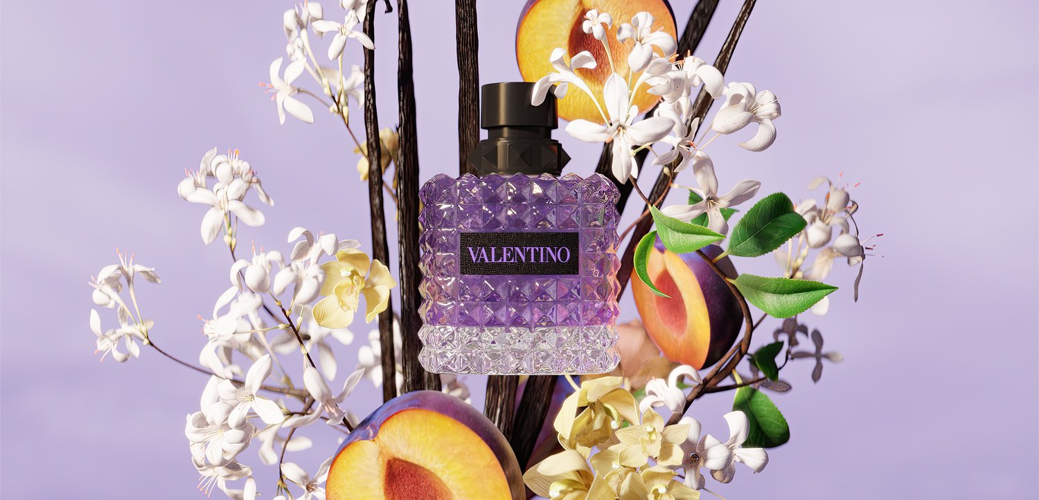 Paars Valentino parfumflesje omringd door witte bloemen en gehalveerde perziken op een lichtpaarse achtergrond.