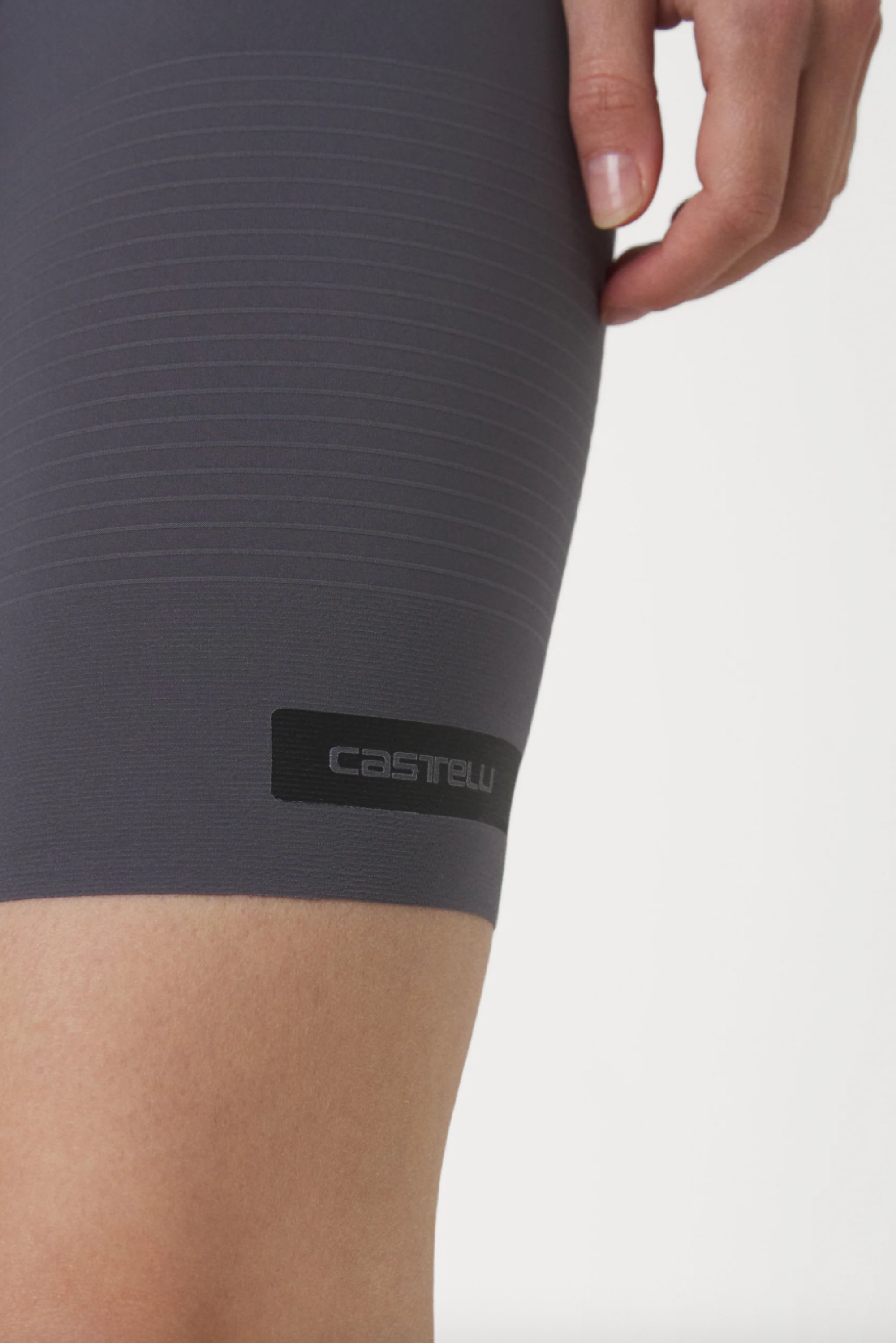 Nahaufnahme des Oberschenkels einer Person, die graue Sportshorts mit strukturiertem Muster und einem schwarzen Etikett mit dem Wort "CASTEL" trägt.