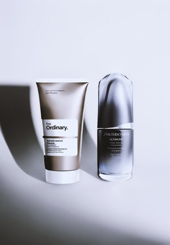 Le masque à l'acide salicylique 2 % de The Ordinary dans un tube doré mat, et Shiseido Men Ultimune, une bouteille semi-transparente noire avec un bouchon arrondi.