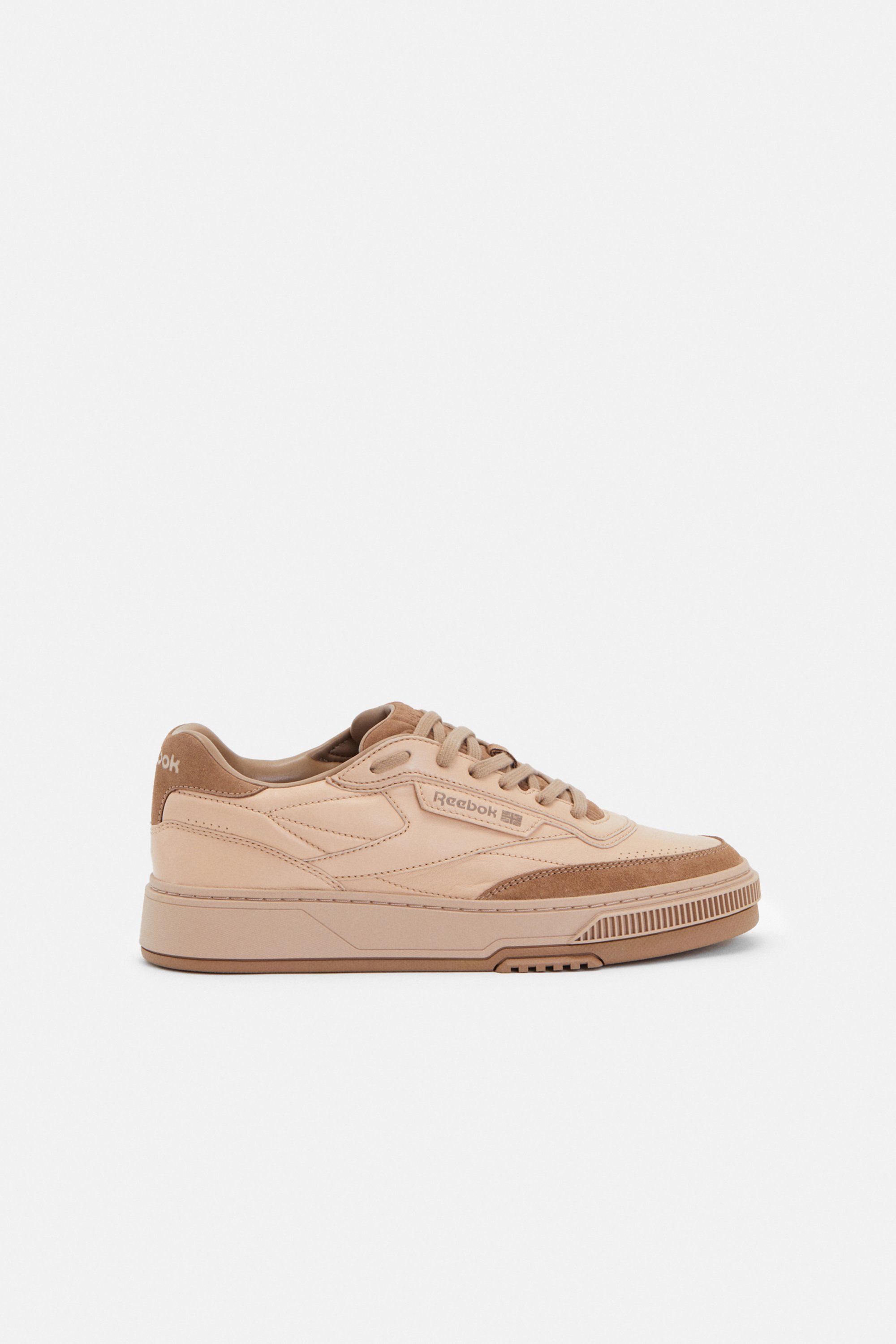 Beige Reebok trainers with a low profile, textured panels, and laces, set against a plain white background.