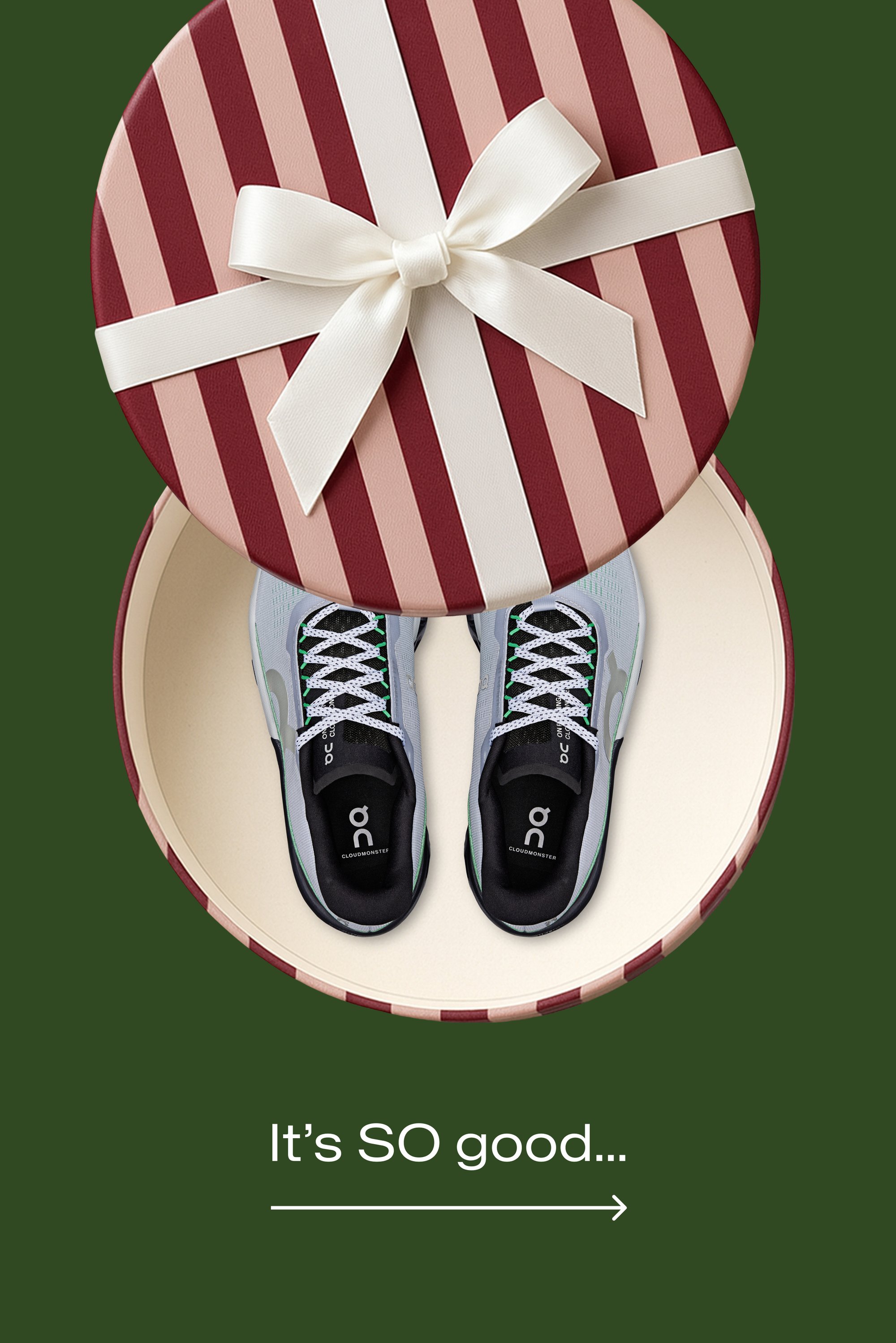 Zapatillas deportivas grises con detalles negros, cordones blancos y partes superiores texturizadas, colocadas dentro de una caja de regalo redonda con rayas granate y rosas.