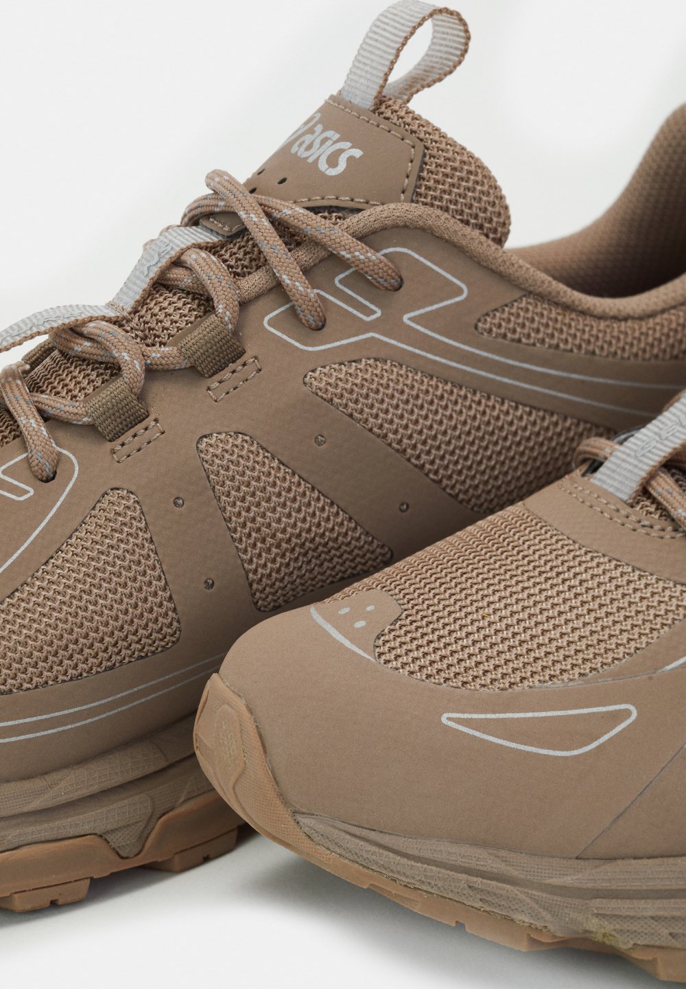 Bruine sportschoenen met netdetails en reflecterende accenten, voorzien van veters en merknaam op de tong, dicht bij elkaar gepositioneerd.