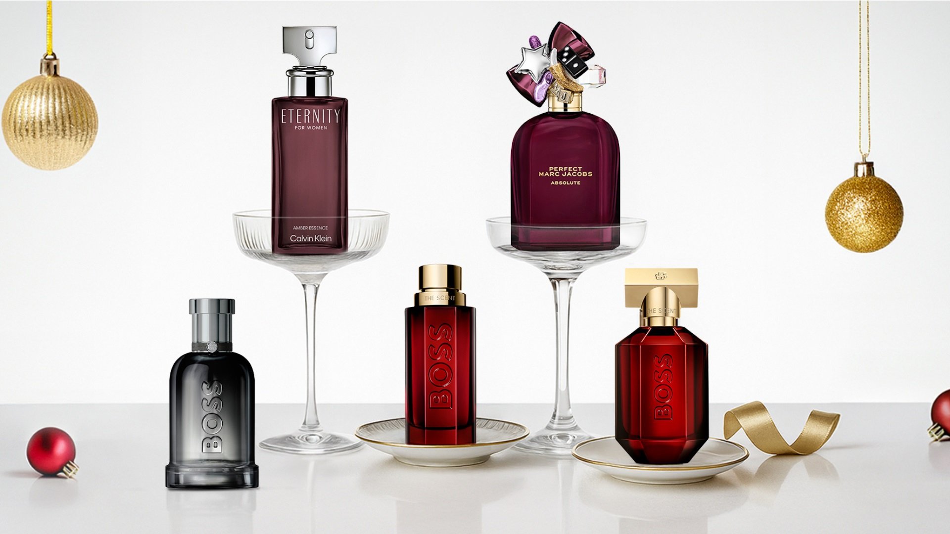 Fem parfymeflasker arrangert med juledekorasjoner. Inkluderer ulike former: klare, avrundede og kantete, med farger som svart, burgunder, gull og gjennomsiktig.