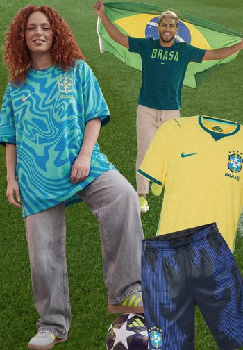 Frau in blau gemustertem Brasilien-Trikot steht auf einem Fußball, Mann dahinter hält brasilianische Flagge, gelbes Trikot und blaue Shorts sind in der Nähe zu sehen.