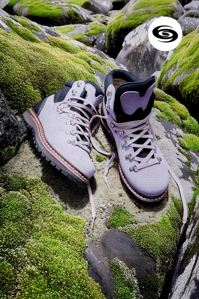 Purple hiking boots with black accents rest on moss-covered rocks, showcasing detailed laces and rugged soles, amidst a natural setting.