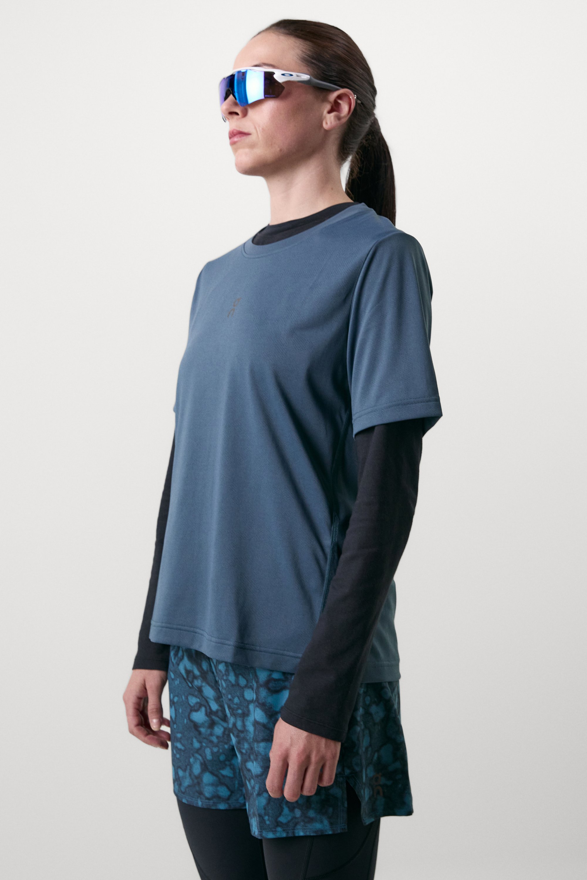 Athletic outfit featuring a blue short-sleeve shirt, black long-sleeve layer, and patterned blue shorts. Accessories include reflective sunglasses.