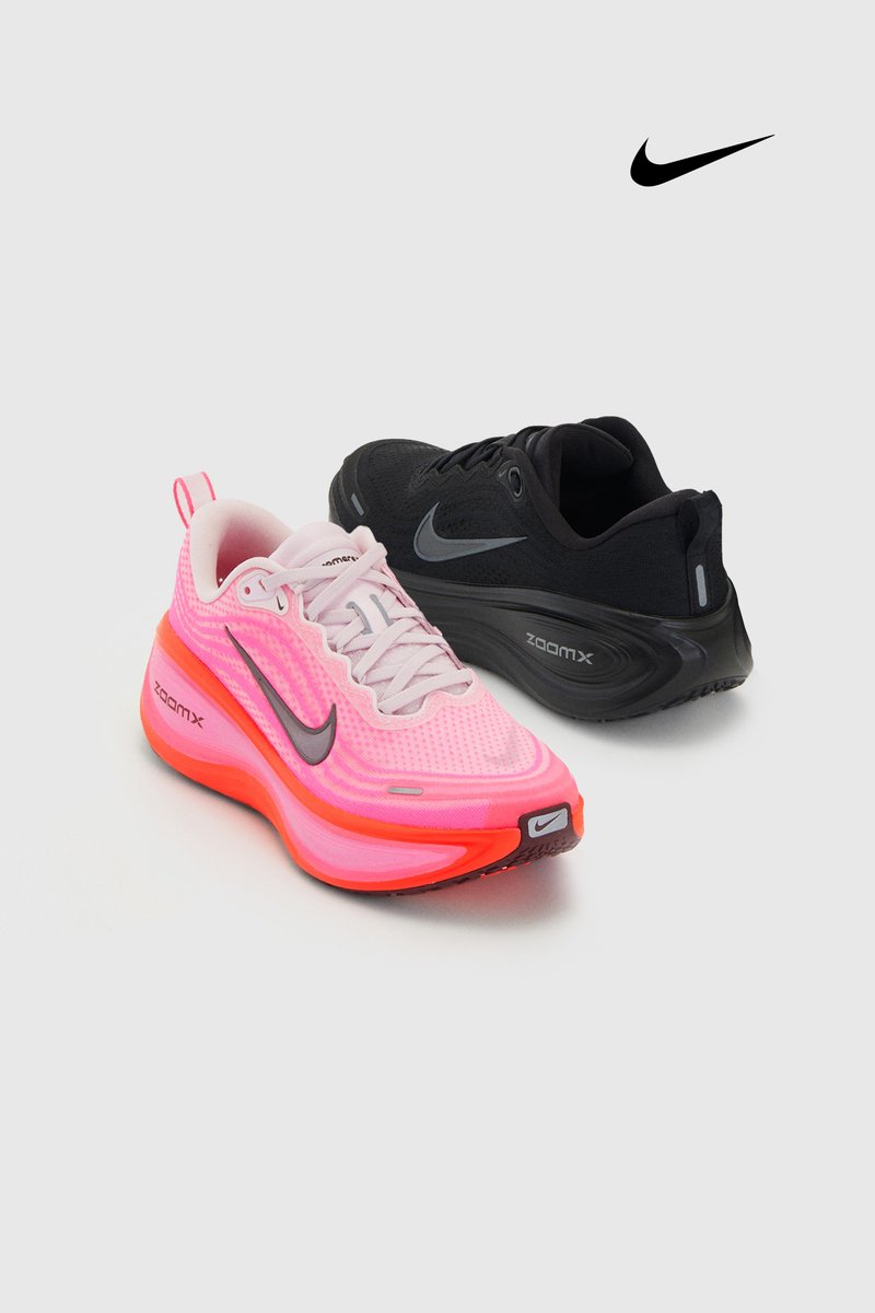 Fel roze en zwarte Nike ZoomX hardloopschoenen met reflecterende swoosh-logo's op een lichtgrijze achtergrond.