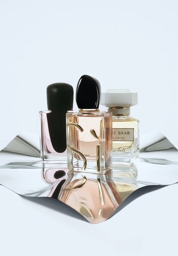 Tre parfymer på reflekterande yta: en med en mattsvart kork, en annan med en rosa vätska och guldaccenter, och en flaska med vit kork.