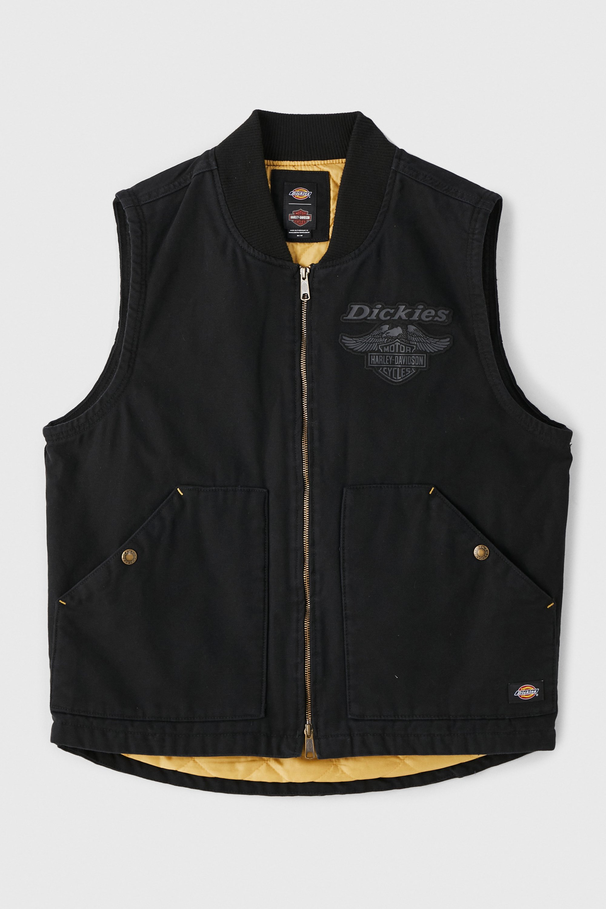 Zwarte mouwloze vest met een rits, twee voorkezen, gouden voering en het "Dickies" logo op de borst, weergegeven tegen een witte achtergrond.