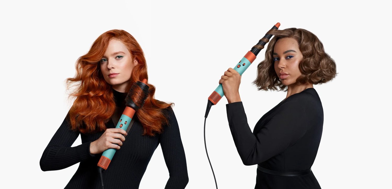 Zwei Frauen, eine mit langen roten Haaren und die andere mit gestylten braunen Locken, halten jeweils ein farbenfrohes Haarstyling-Werkzeug und präsentieren verschiedene Frisuren.