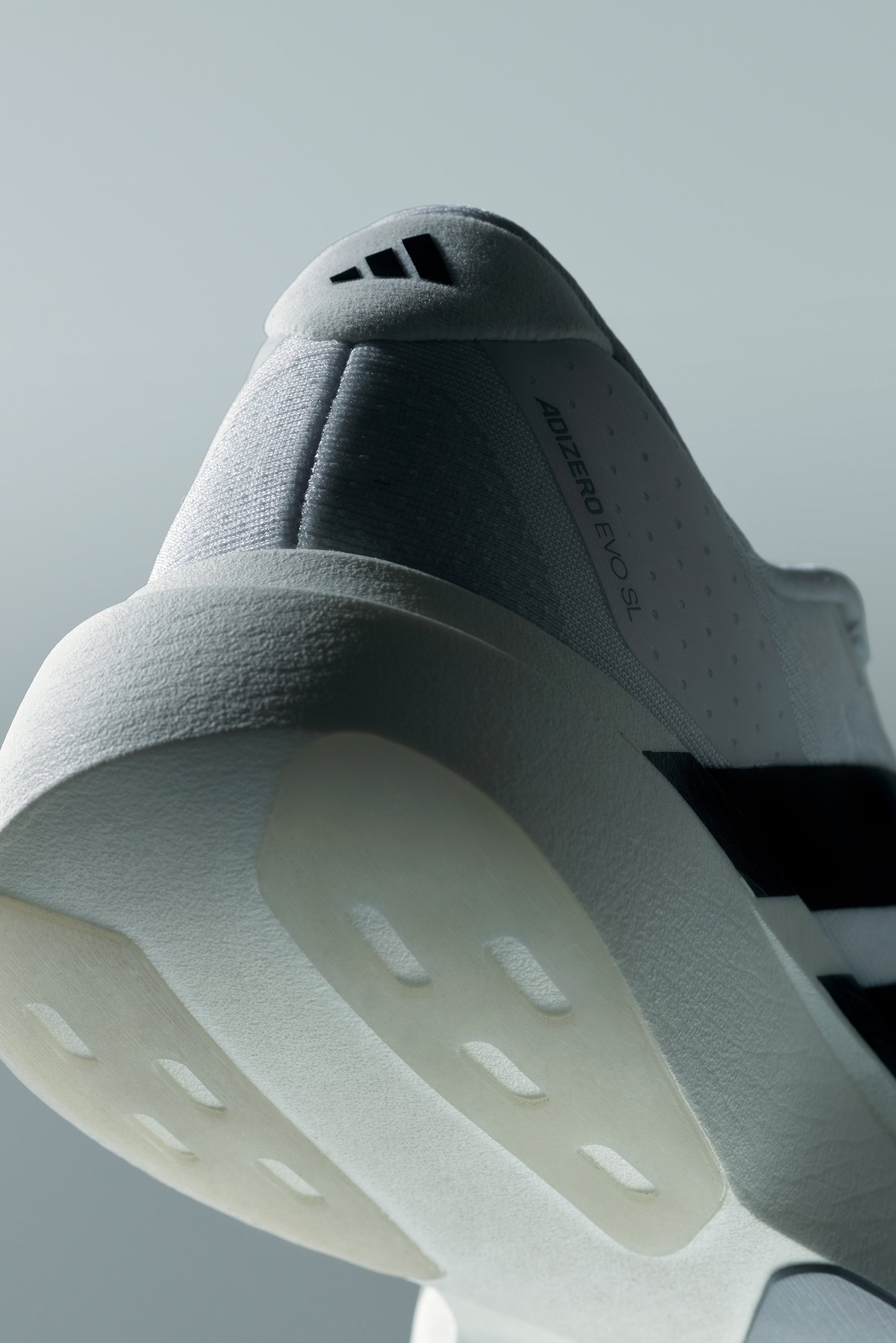 Close-up of a white sneaker's sole, showcasing textured upper materials, a sleek design, and the Adidas logo on the heel.