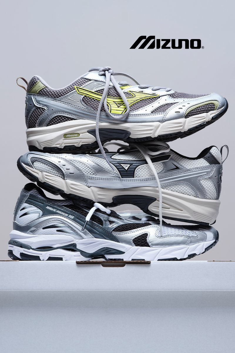 Tres pares de zapatillas de correr Mizuno apiladas verticalmente, con diseños en gris y plata con acentos y cordones neón.