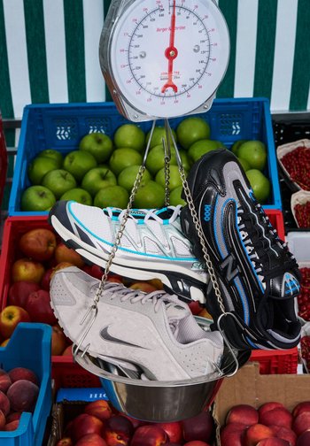 Trois paires de chaussures de sport exposées sur une balance : blanches avec des accents turquoise, grises avec une surface texturée et noires avec des détails bleus.