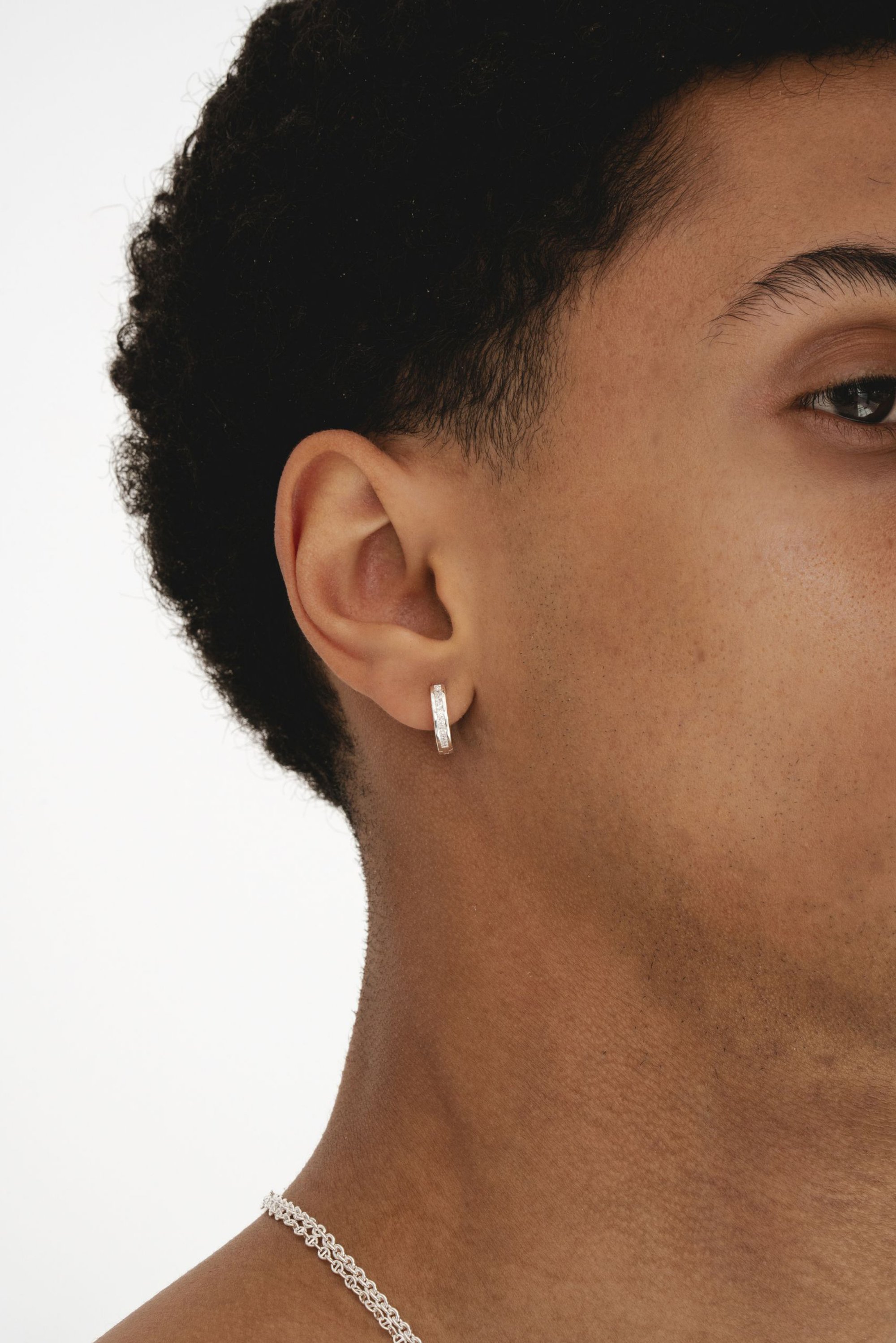 Pendiente de aro de plata con una superficie texturizada, exhibido en la oreja de un modelo con cabello corto y rizado. Diseño simple y elegante.