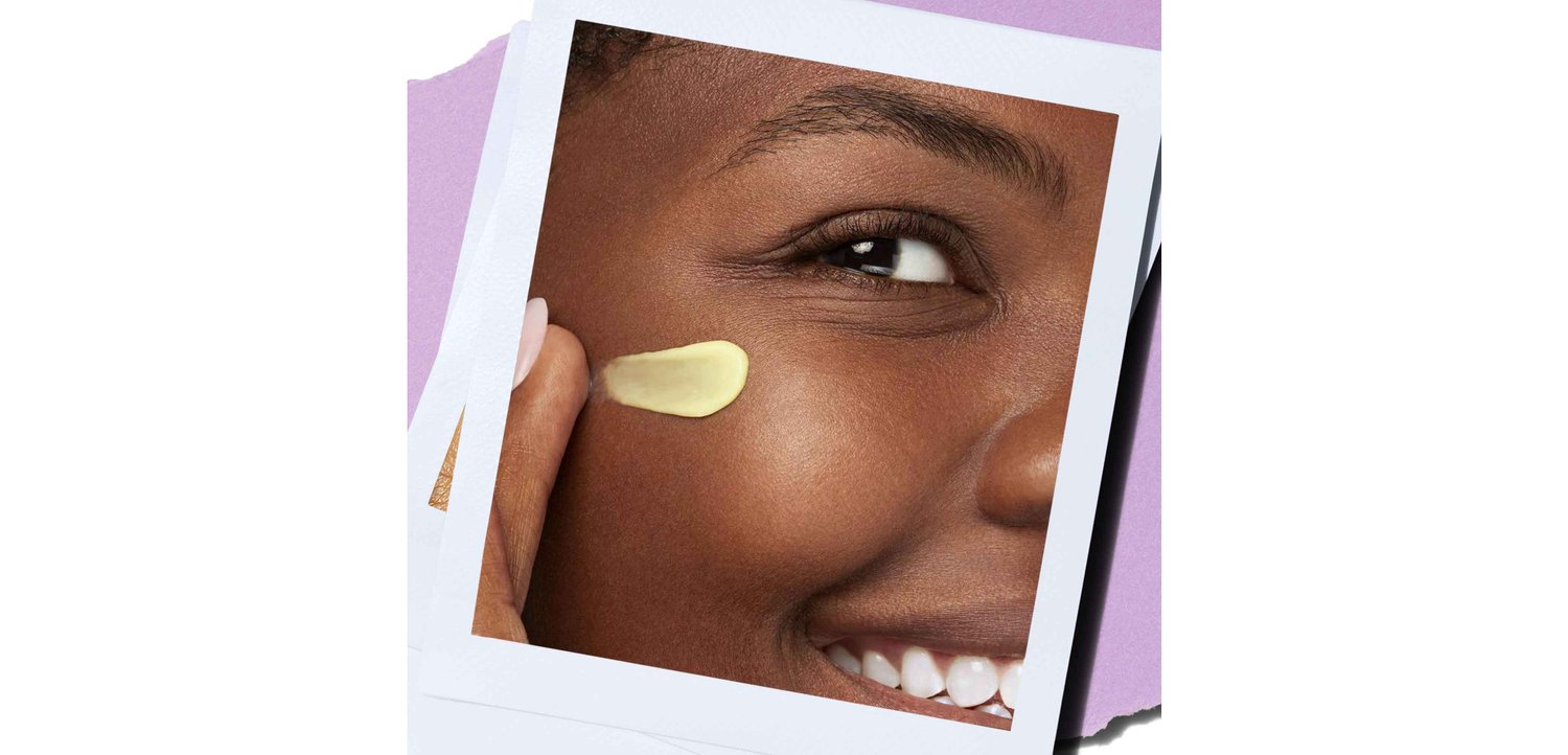 Lächelnde Person, die eine gelbe Creme auf ihre Wange aufträgt, im Close-up mit weißen Rändern auf einem lila Hintergrund.