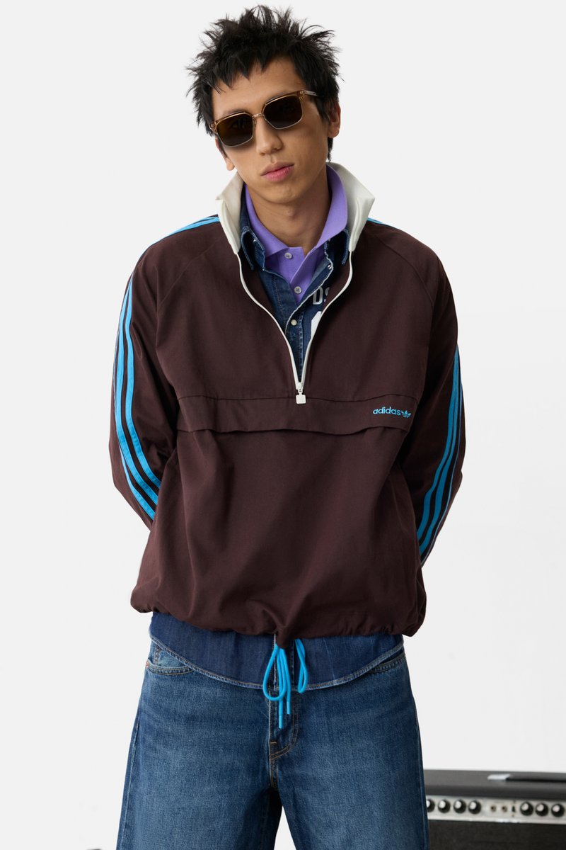Brauner Polyester-Pullover mit weißem Kragen und blauen Streifen. Leicht tailliert mit einem blauen Zugband. Getragen über einem lila Hemd.