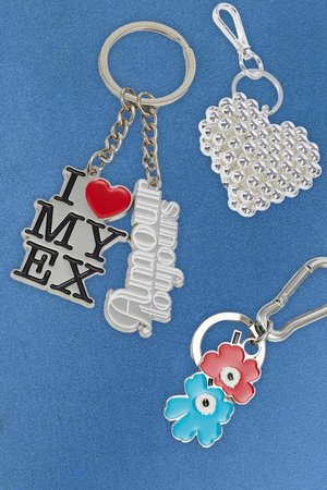Cuatro llaveros: uno con "I ❤️ MY EX" en negro y rojo, uno en forma de corazón plateado con rhinestones, y dos flores en azul y rojo en un anillo plateado.