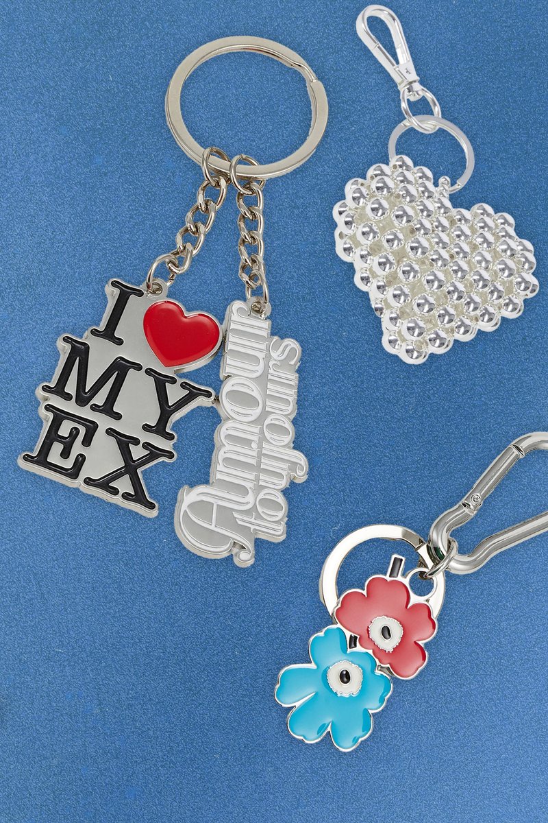 Vier sleutelhangers: één met "I ❤️ MY EX" in zwart en rood, één zilveren hart met strasssteentjes, en twee bloemen in blauw en rood aan een zilveren ring.