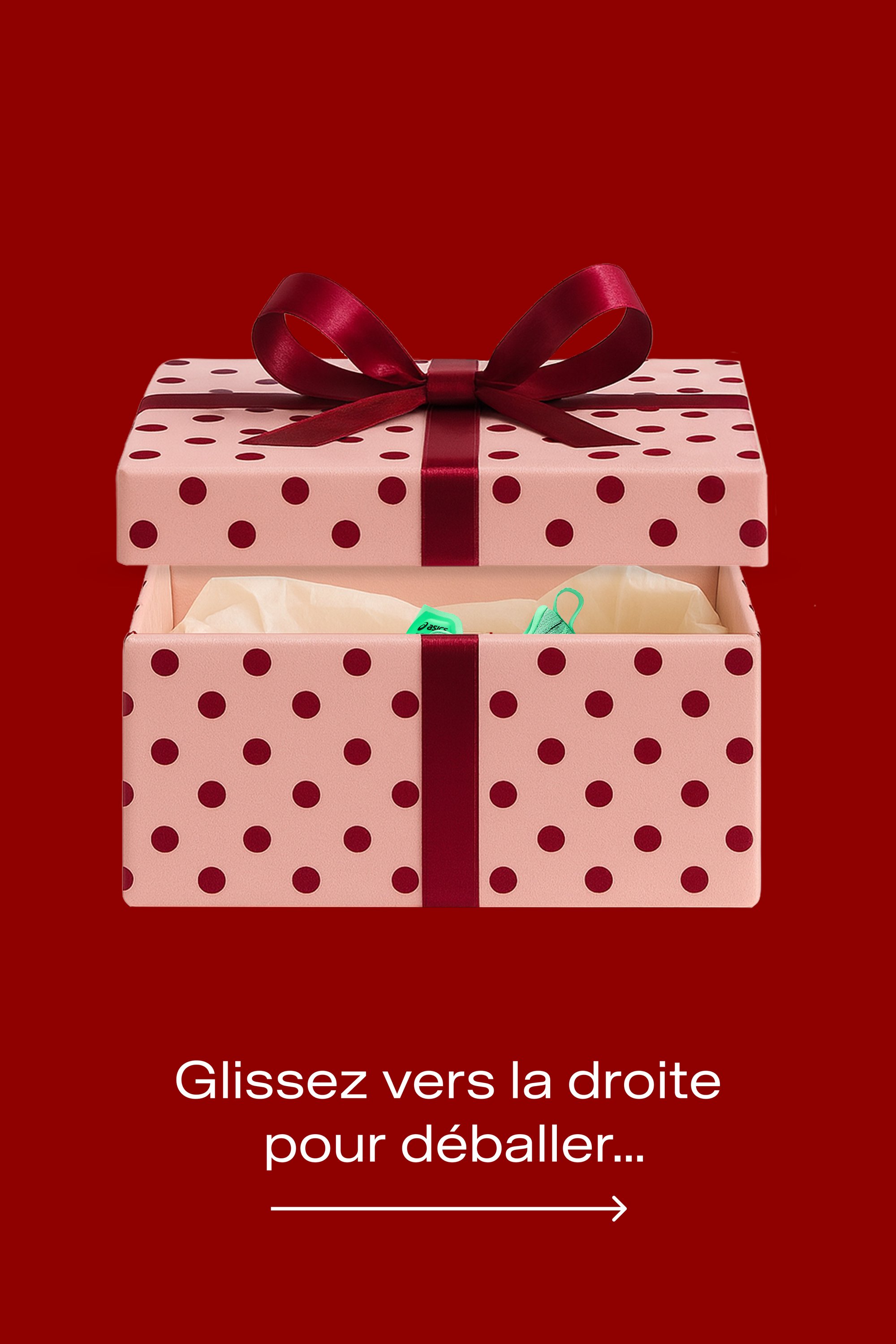 Boîte cadeau rose à pois rouges, ornée d'un ruban en satin rouge foncé. Partiellement ouverte pour révéler un papier de soie de couleur claire à l'intérieur.