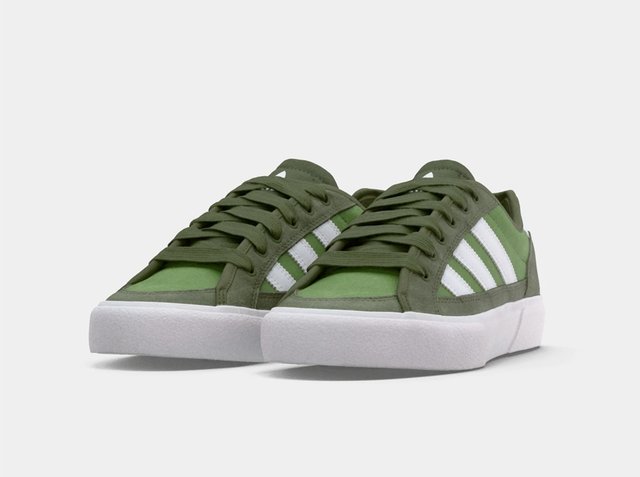 Pair of low-top green sneakers with white stripes and thick white soles, viewed from the front-left angle on a light background.