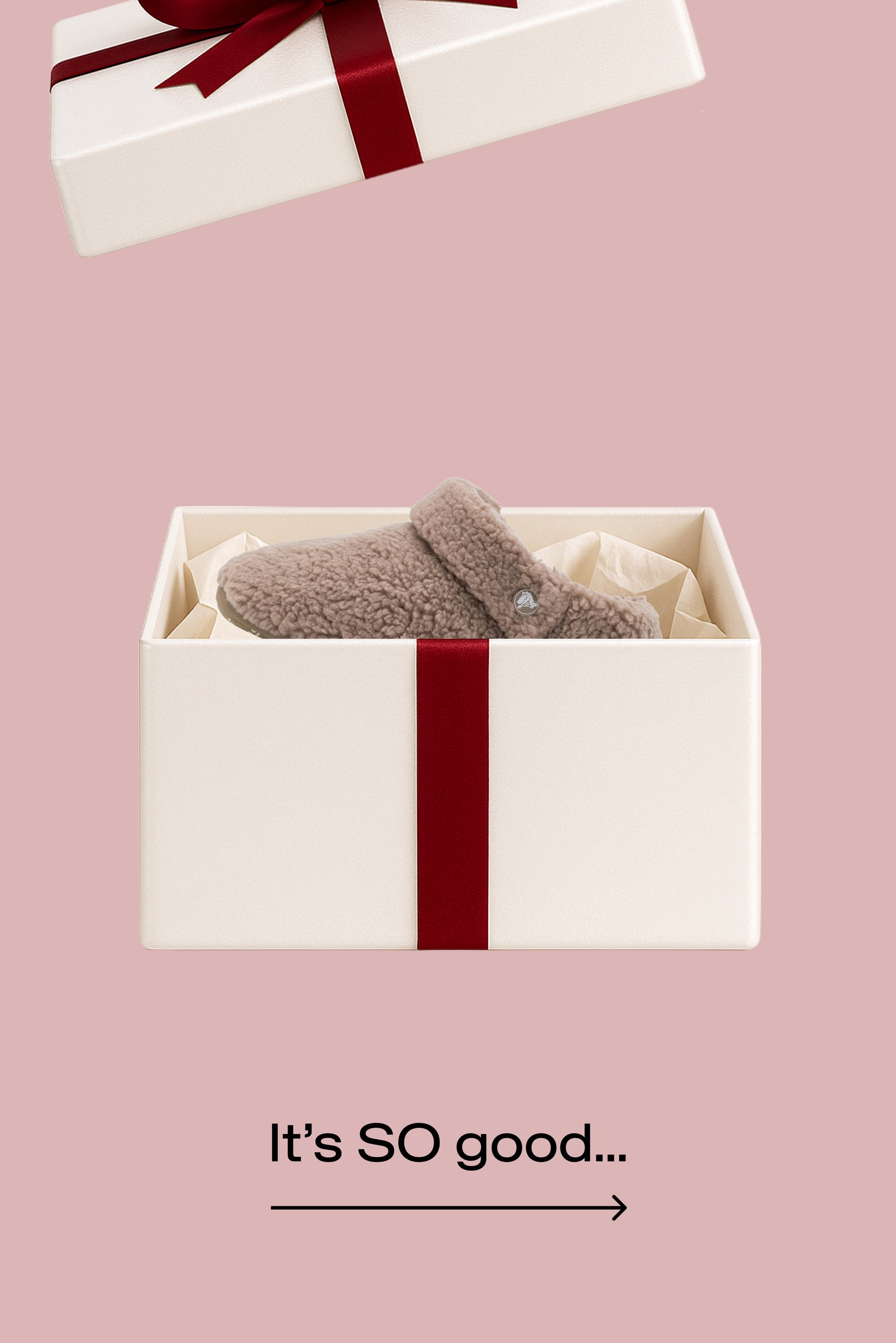 Weicher brauner Fleece-Hausschuh in einer offenen cremefarbenen Geschenkbox mit rotem Band vor einem rosa Hintergrund, darunter der Text "Es ist SO gut...".