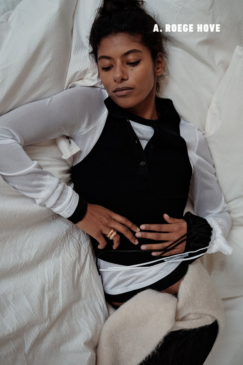 Zwart geribd top met lange mouwen onder een witte, doorschijnende top, geaccentueerd met een gouden ring en een crèmekleurige fleece losjes gedrapeerd.