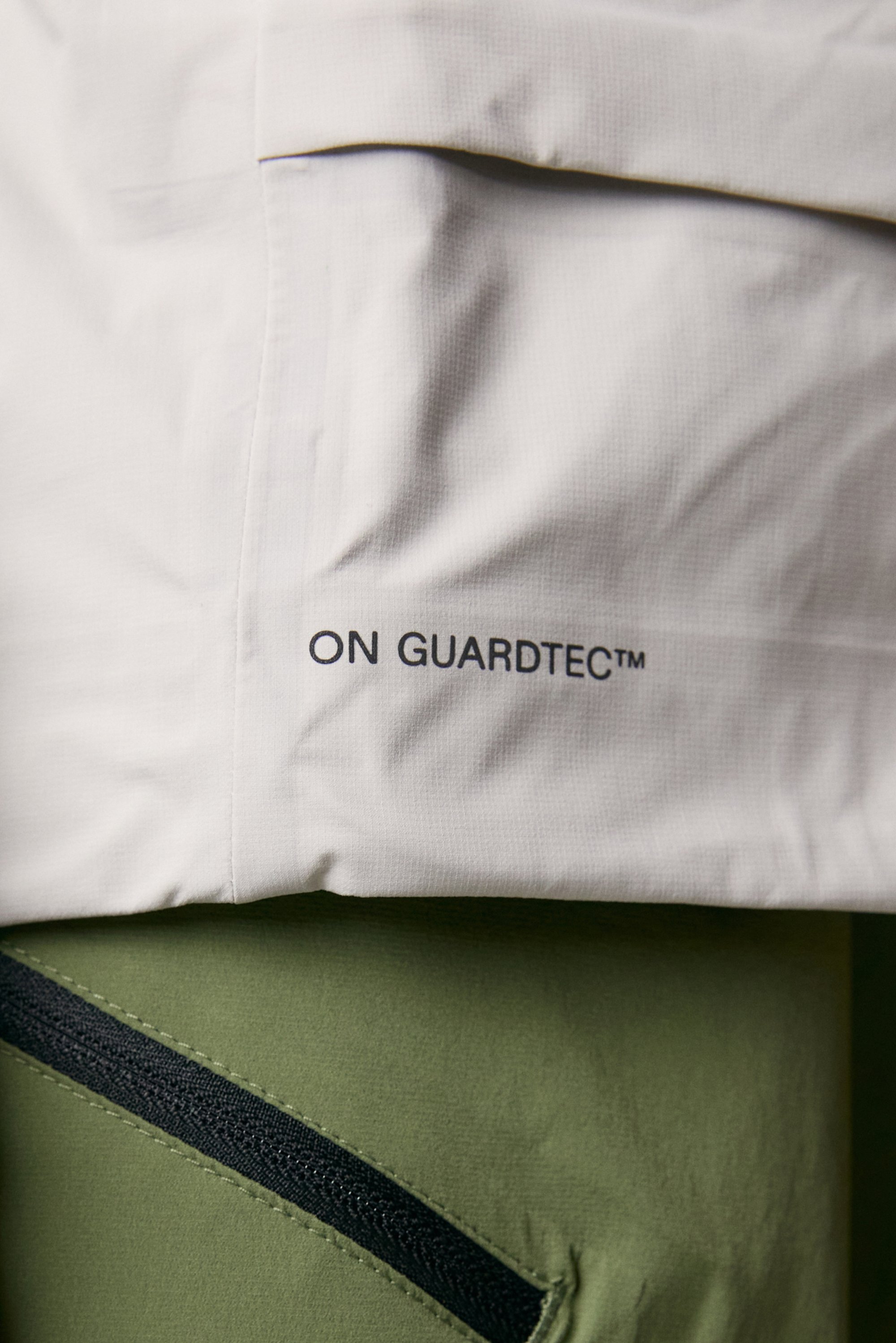 Light gray upper garment with "ON GUARDTEC™" logo, positioned above an olive green lower garment featuring a black zipper pocket.