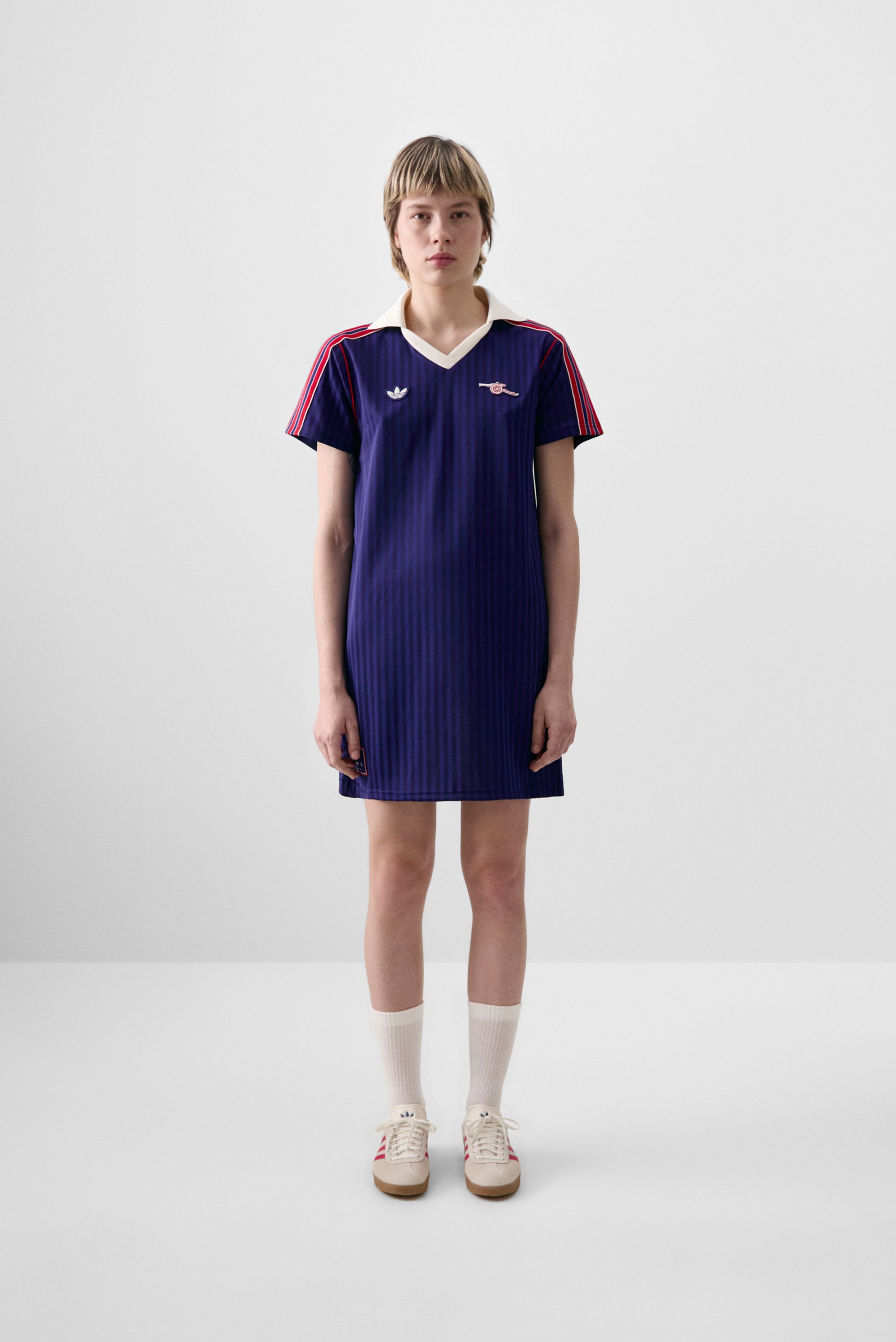 Marineblauwe gestreepte jurk met een witte kraag, korte mouwen versierd met rood. Draagt crèmekleurige sneakers en witte sokken. Bevat merklogo's.