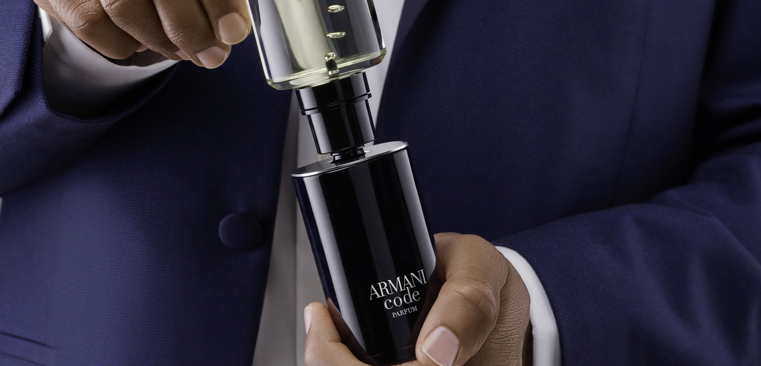 Person in navy suit holding and removing cap from a black Armani Code parfum spray bottle.