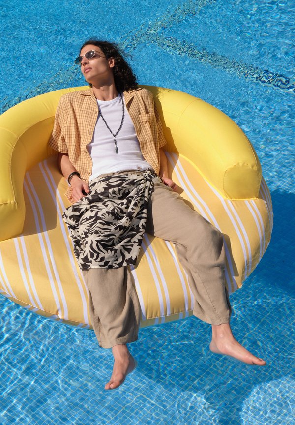 Jeune personne portant des lunettes de soleil se détendant sur un flotteur gonflable rayé jaune dans une piscine bleue claire.