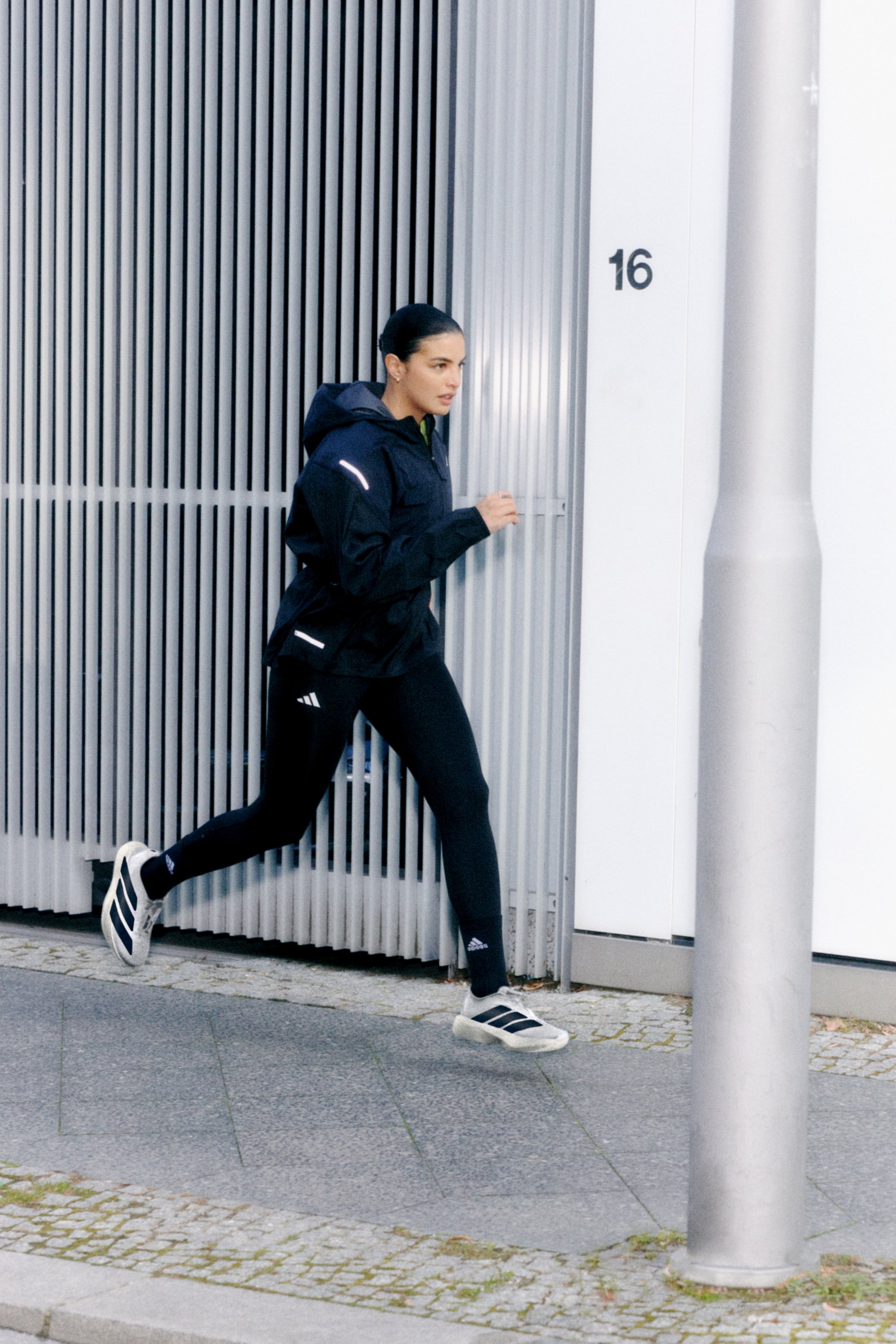 Una mujer con ropa deportiva corre past una edificio con paneles grises verticales y una farola, centrada en su ejercicio.
