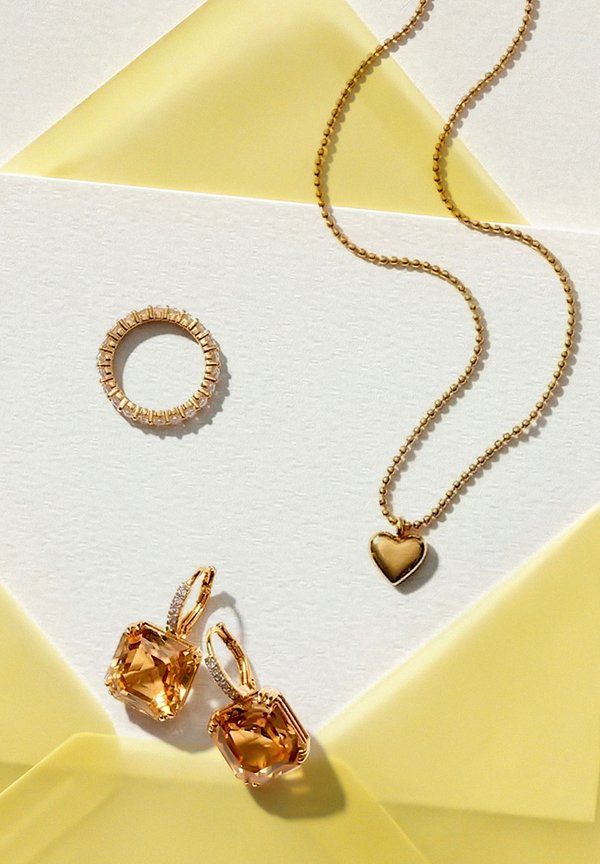 Gold ring, heart pendant necklace with beaded chain, and a pair of gold earrings featuring large amber gemstones on a white and yellow paper background.