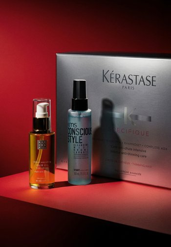 To hårpleieprodukter: en ravfarget olje i en pumpeflaske og en blå mist spray i en gjennomsiktig flaske, sammen med en grå Kérastase-boks.