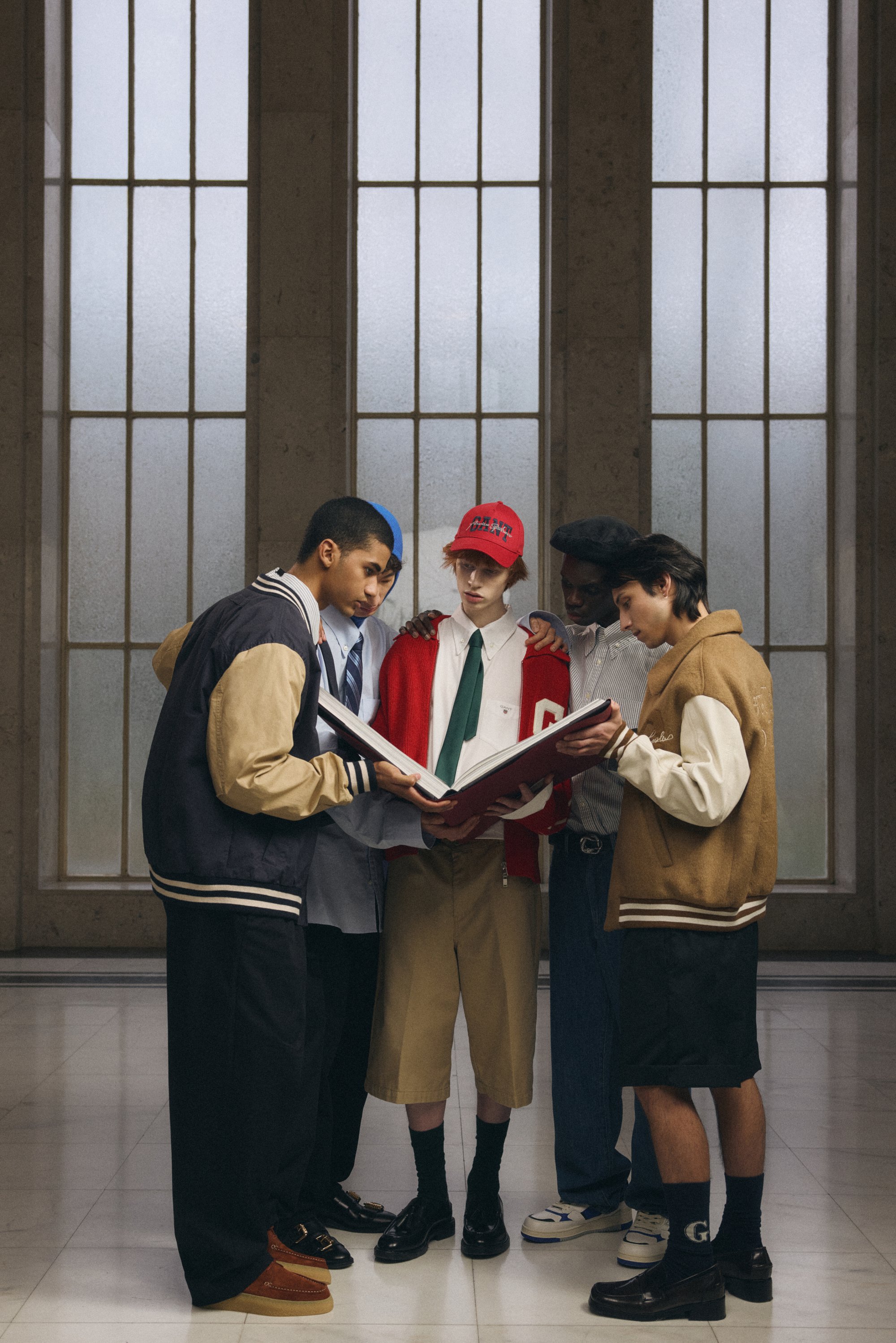 Fyra mångsidiga unga människor samlas runt en öppen bok och delar en stund av diskussion. Höga fönster lyser upp deras avslappnade kläder och uttryck.