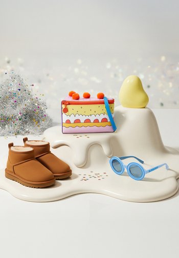 Barna nubuk boka csizma, színes tasak pom-pomokkal, kék, kerek napszemüveg és egy sárga dísztárgy fényes felületen.