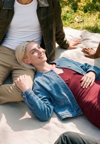 Una donna con i capelli biondi sorride mentre è sdraiata su una coperta all'aperto con la testa appoggiata sulle ginocchia di una persona.