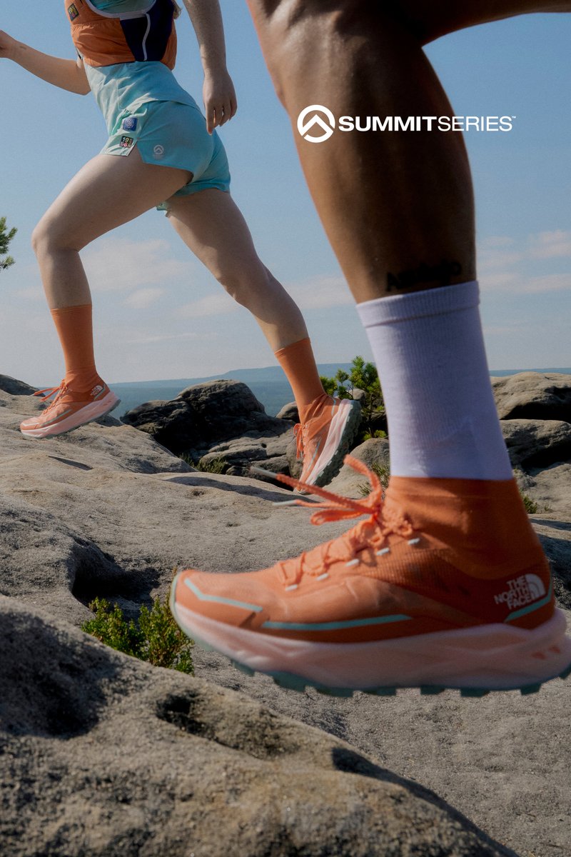 Two runners wearing orange shoes and socks hiking on rocky terrain under a clear sky, with a distant mountain view and Summit Series logo.