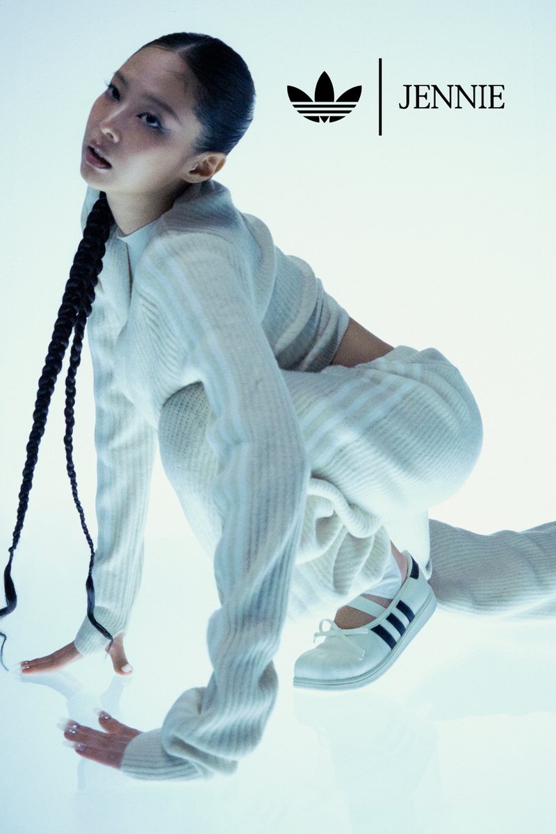 Woman in white ribbed outfit crouches on reflective floor wearing white Adidas shoes with black stripes, braided hair, with Adidas logo and text "JENNIE".