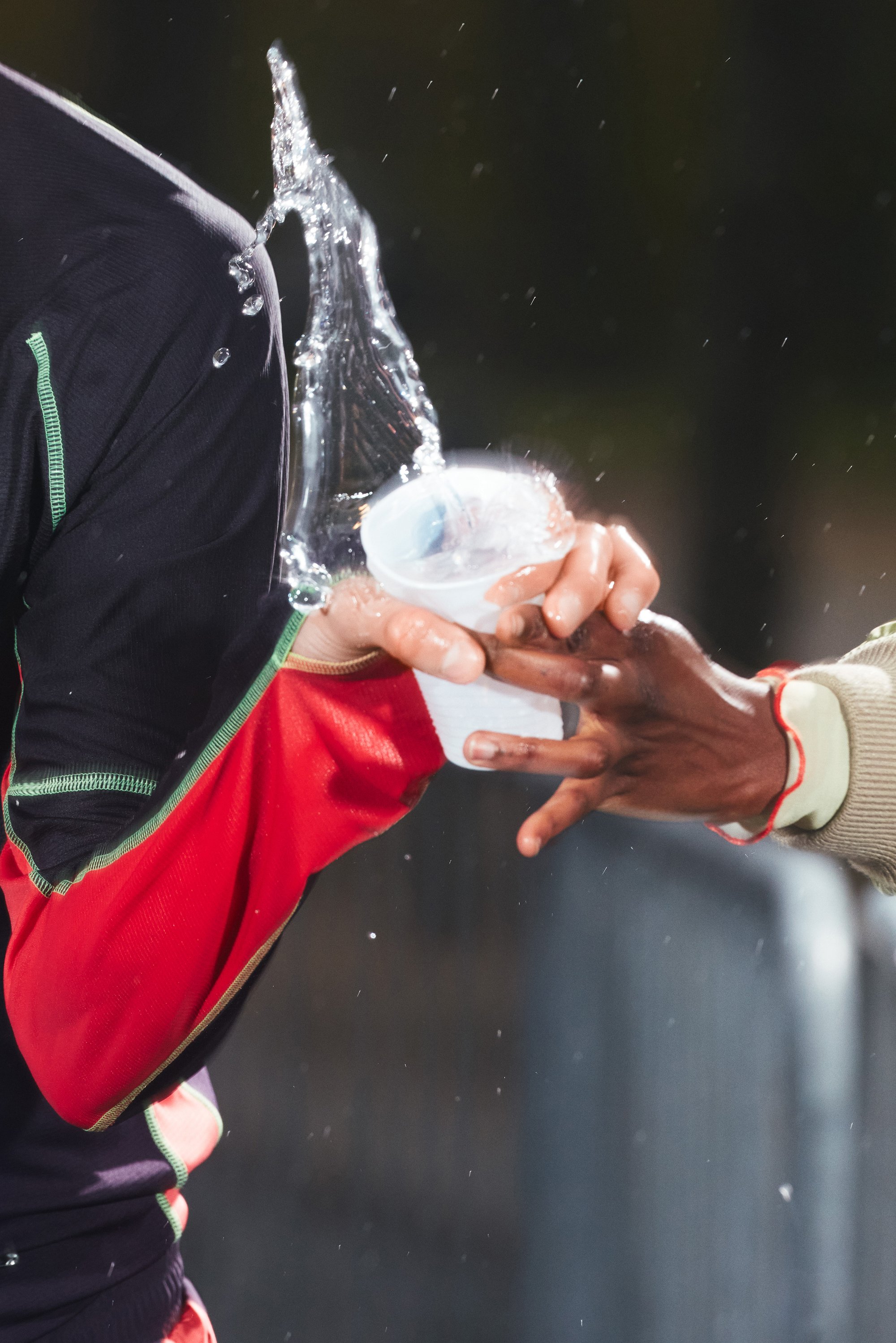El agua salpica de una copa mientras una mano se extiende hacia otra en un momento dinámico, mostrando emoción y trabajo en equipo en el deporte.
